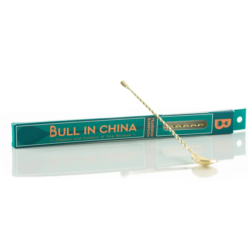 A teardrop-shaped barspoon with a gold-colored tip, packaged in a green and white box with 'BULL IN CHINA' printed in black text.
