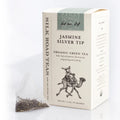 Silk Road Teas Jasmine Silver Tip organic green tea box in cream packaging with a sage green top panel, shown next to a single tea bag containing loose tea leaves on a white background.