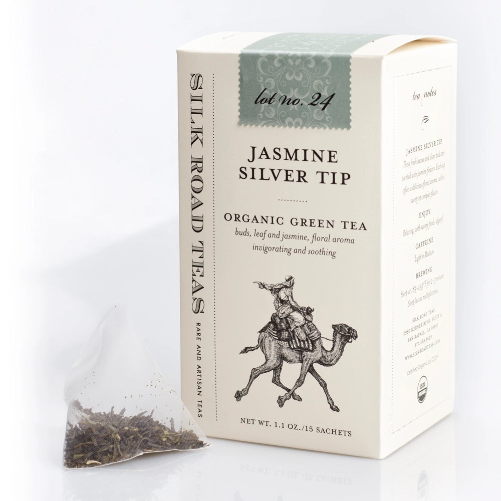 Silk Road Teas Jasmine Silver Tip organic green tea box in cream packaging with a sage green top panel, shown next to a single tea bag containing loose tea leaves on a white background.