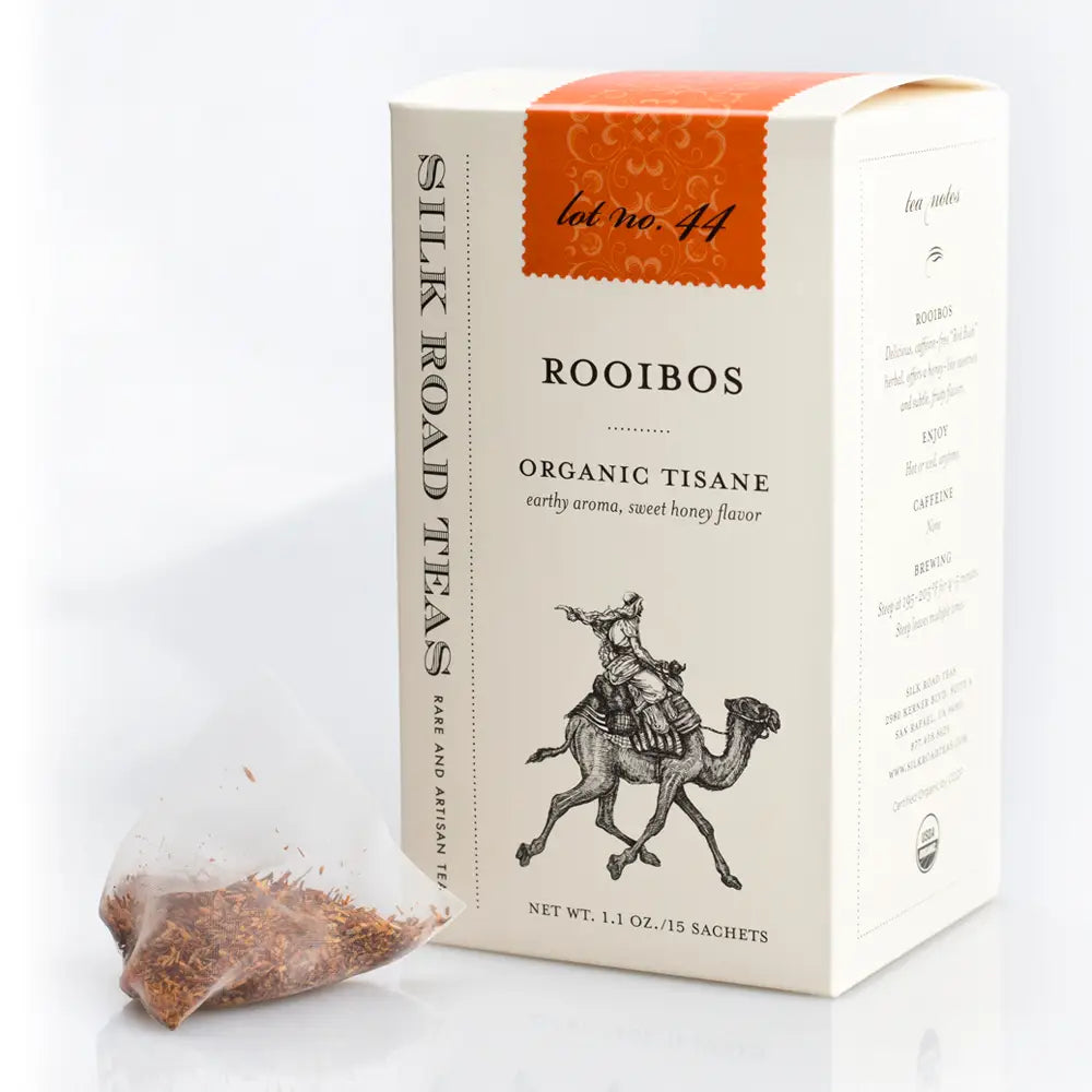 A box of Silk Road Tea's Rooibos Organic Tisane tea, shown with a single clear teabag containing loose-leaf tea in the foreground on a white background.