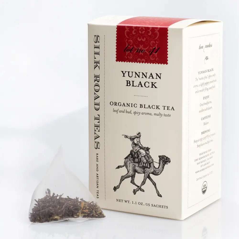 A box of Silk Road Teas Yunnan Black Organic Black Tea next to a single bag of loose-leaf tea on a white background.